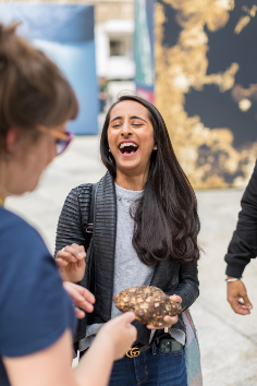 woman with long dark hair laughing and holding a meteorite at the exhibition